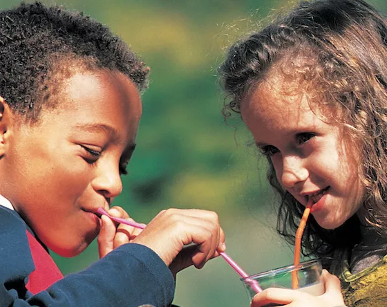 A young boy and girl sip chocolate milk together in the sunshine