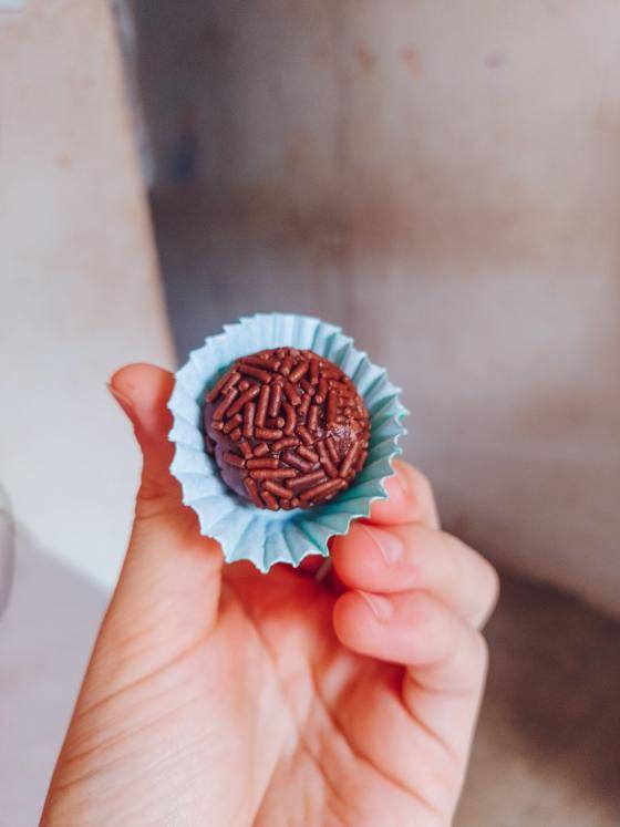 Brigadeiro de chocolate em forminha azul claro sendo seguro em uma mão