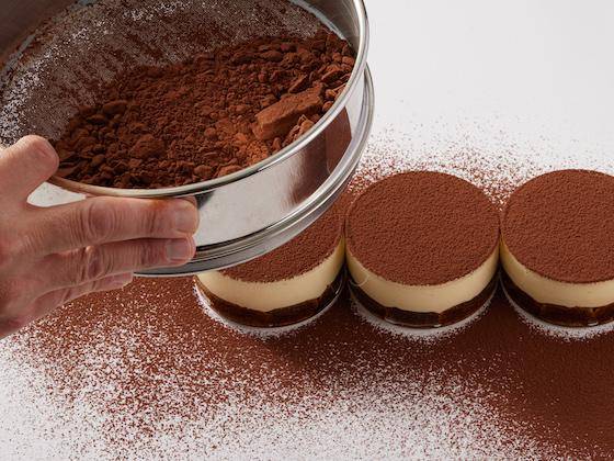 Cacao Powder being sifted over individual Tiramisu